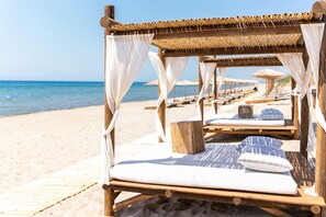 Una playa con sillas de madera y sombrillas de paja.