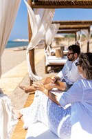 Una pareja sentada en un banco de madera bajo una pérgola en un resort frente al mar.