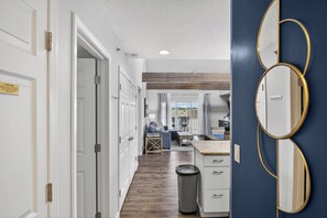 A hallway leading to a dining area with a view of the city, a trash can, and a wall-mounted mirror. - Bridgepointe Condo - Two Bedroom Apartment, Sleeps 6 (Osage Beach)