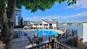 Ein Pool mit Liegestühlen und Sonnenschirmen, umgeben von Gebäuden mit Blick auf ein Gewässer.