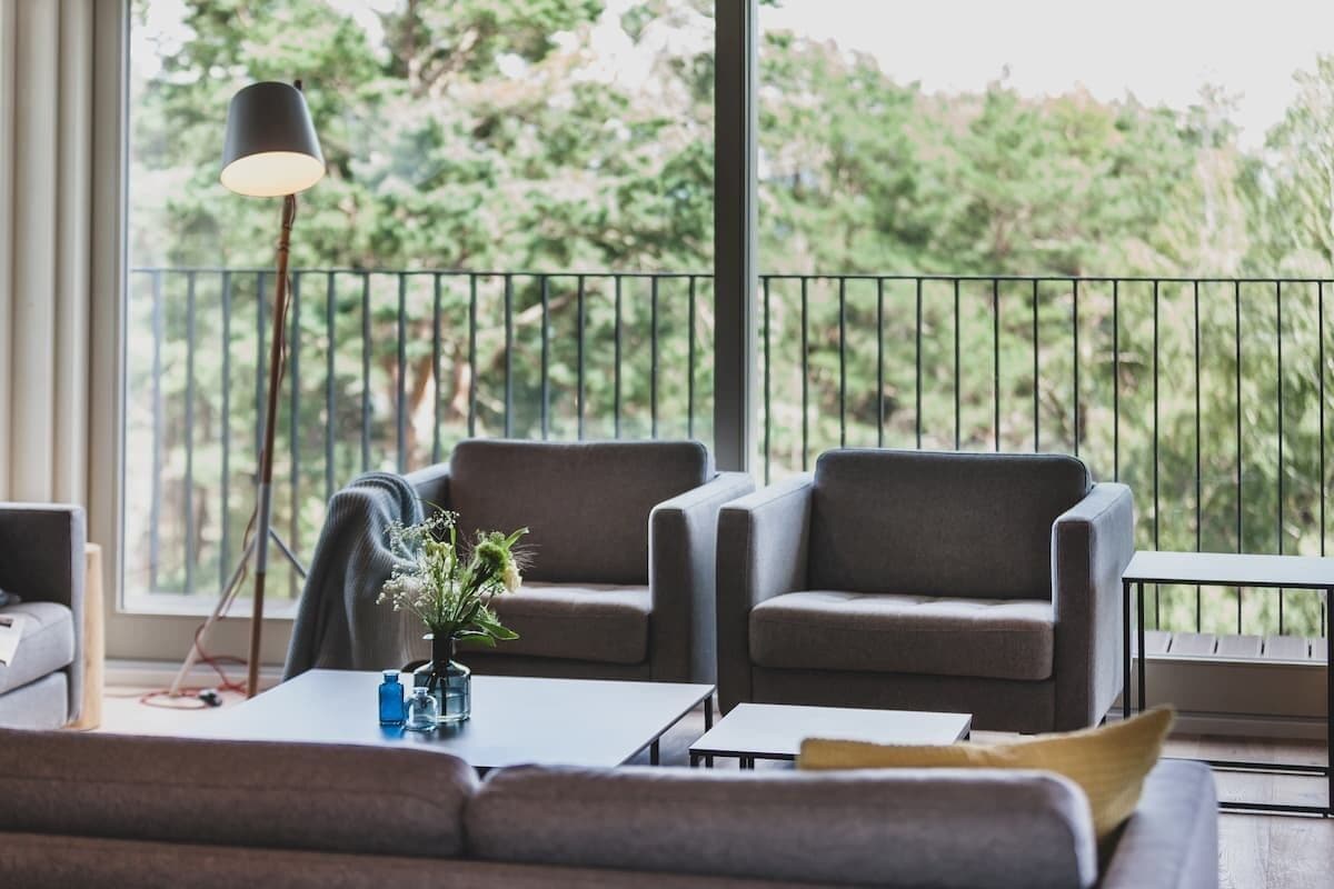 A modern living room with a sofa, two armchairs, a coffee table, and a floor lamp. A balcony with a railing is visible in the background.