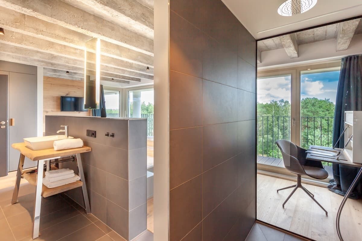 A modern bathroom with a wooden vanity, a large mirror, and a view of a balcony with a chair.