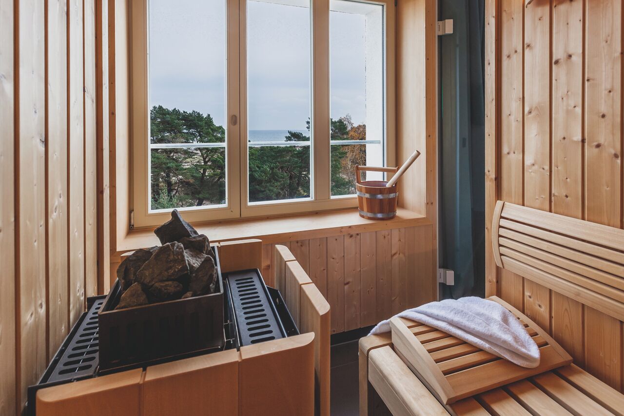 A sauna room with wooden walls and a large window overlooking a forested area.