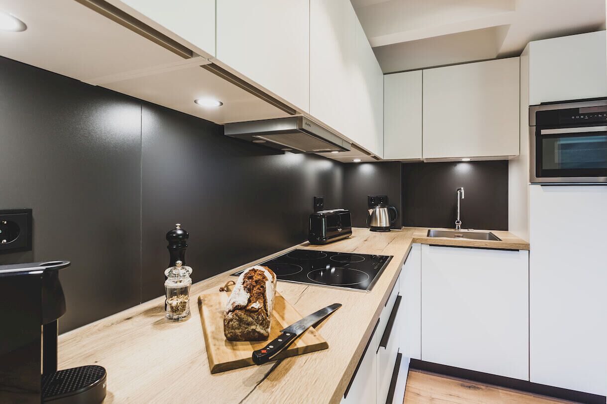 A modern kitchen with a black backsplash, white cabinets, a built-in oven, and a wooden countertop.