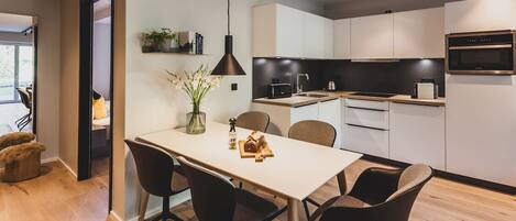 Une cuisine moderne avec des meubles blancs, un plan de travail noir et un four encastré. On y trouve une table à manger avec quatre chaises et un vase de fleurs.