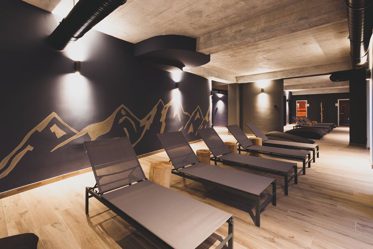A spa room with wooden floors, black walls with mountain designs, and several sun loungers.