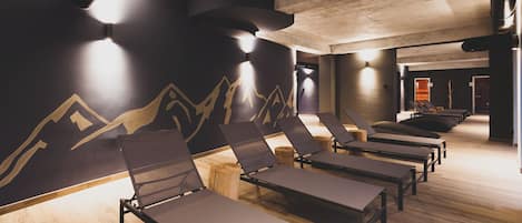 Un cuarto de spa con pisos de madera, paredes negras decoradas con diseños de montañas y varios camastros.