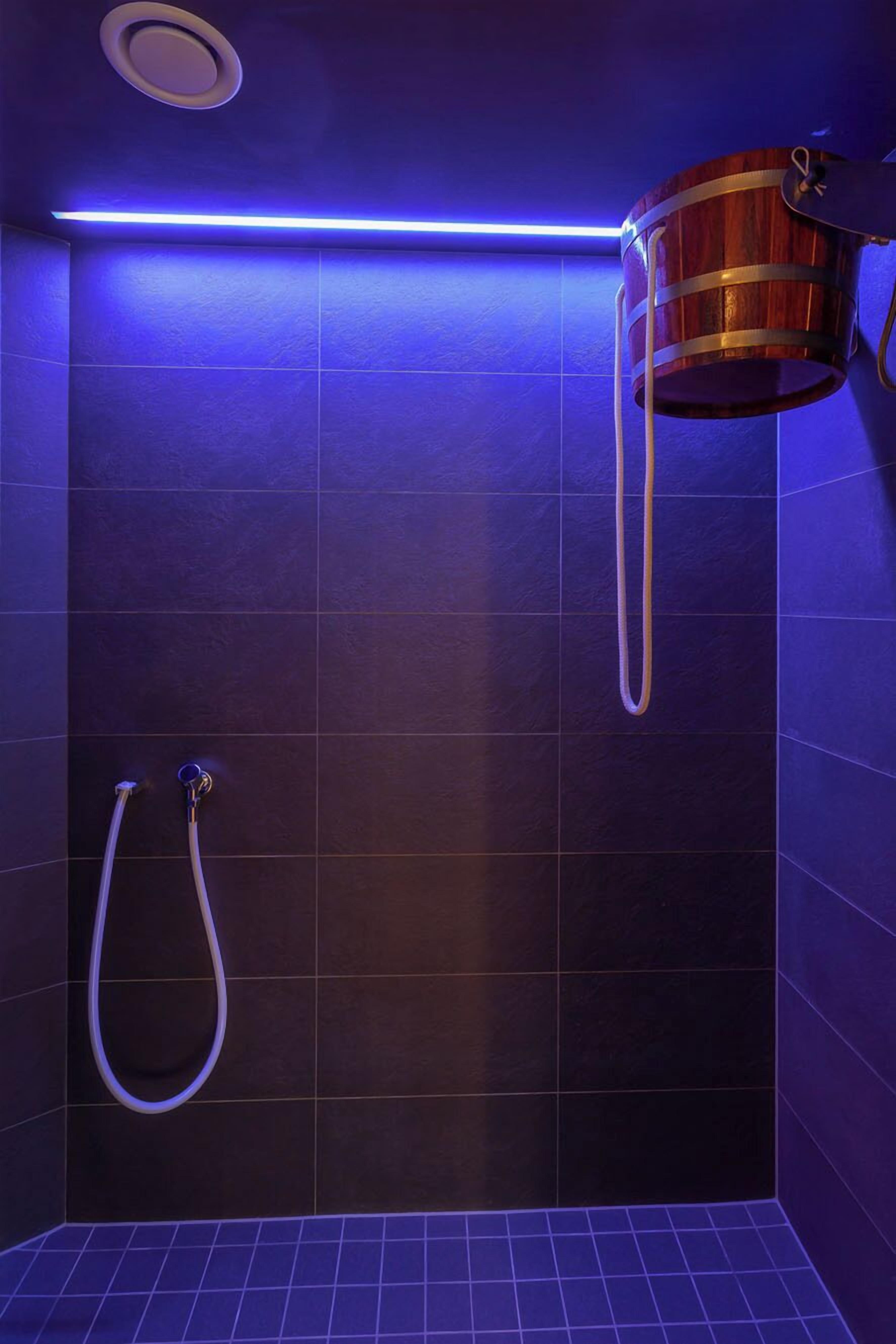 Une douche avec des carreaux de couleur sombre et un seau en bois.