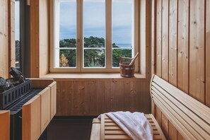 Una sauna de madera con un banco, un balde y una ventana con vistas a un paisaje natural.