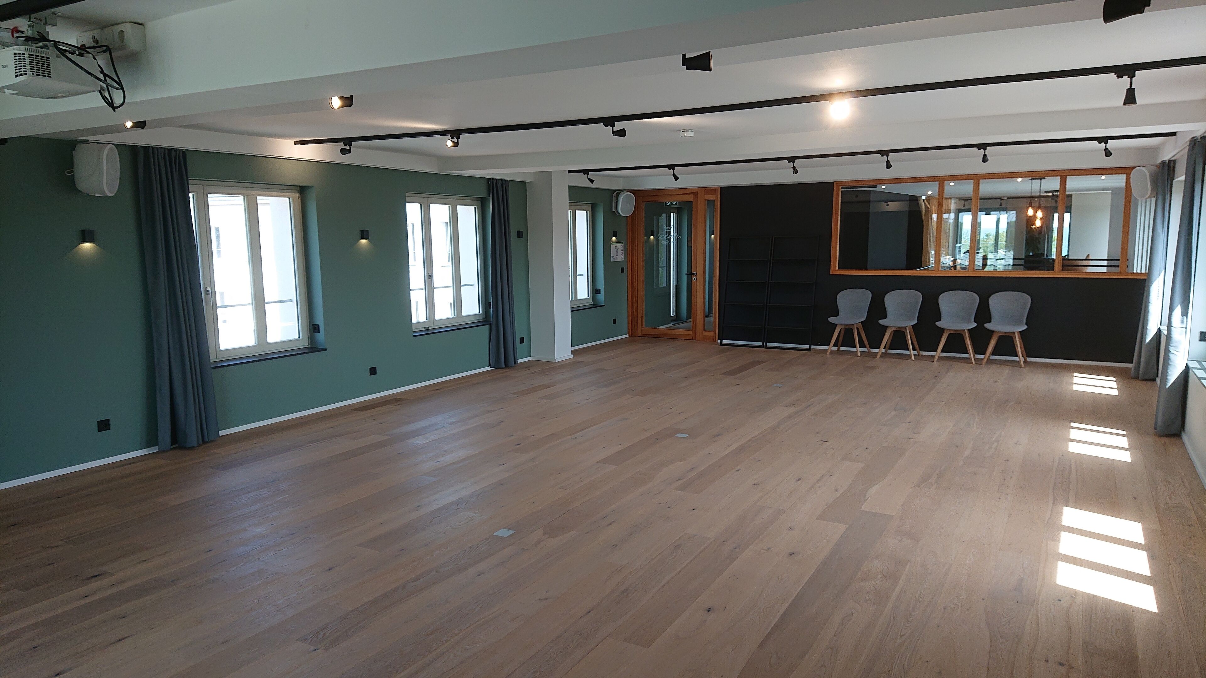 Une pièce spacieuse dotée d’un plancher en bois, de grandes fenêtres et d’un coin salon avec des fauteuils.