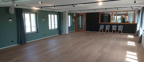 Una habitación amplia con suelo de madera, ventanas grandes y una zona de estar con sillas.