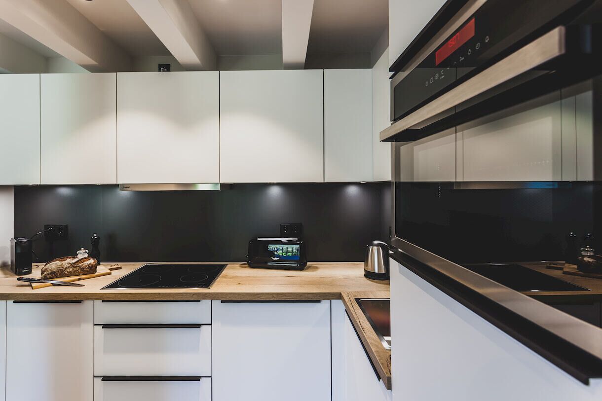 A modern kitchen with white cabinetry, a wooden countertop, a built-in oven, and a digital clock.