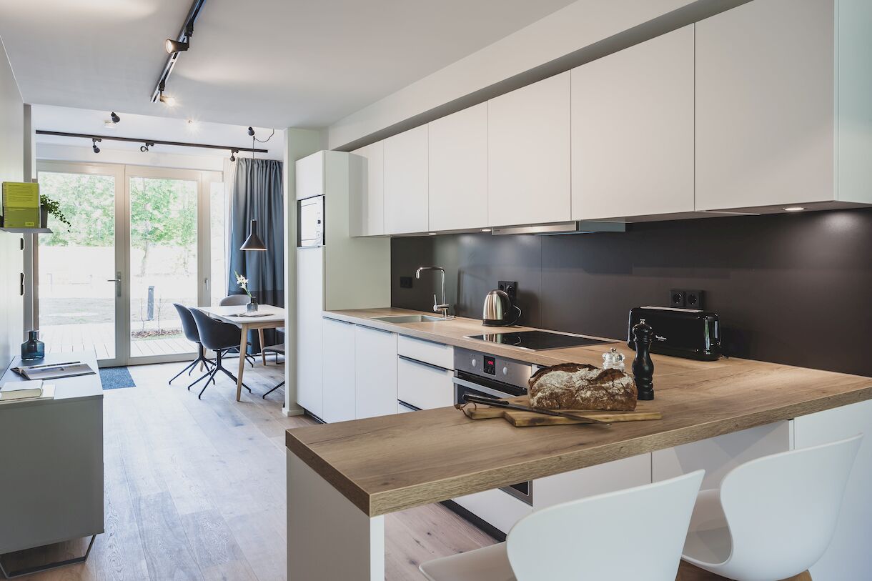 A modern kitchen with white cabinets, a wooden countertop, and a dining area with a table and chairs.