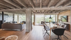 A spacious living area with a large sofa, dining table, and chairs. There is a view of the outdoors through large windows. - Mariandl am Meer (Binz)