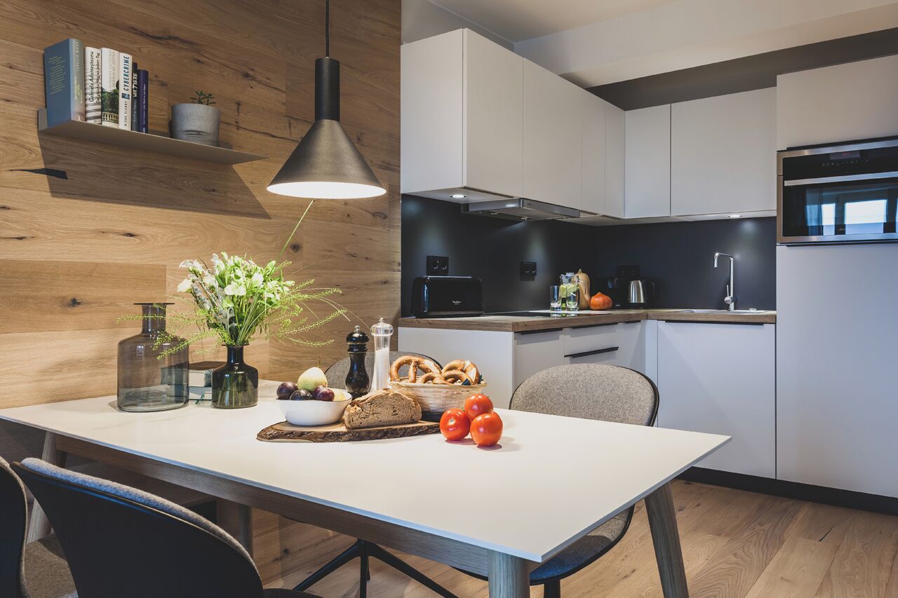 A modern kitchen with white cabinets, a black countertop, and a hanging pendant light.