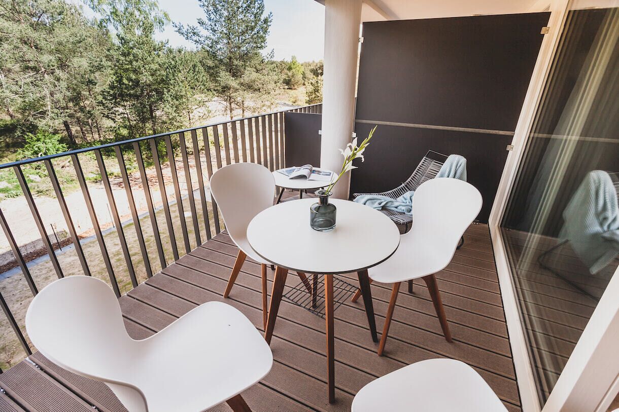 A balcony with a wooden deck, white chairs, and a small table with a vase of flowers.