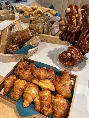 Variedad de productos horneados, incluyendo pan, cruasanes y pretzels, sobre una mesa.