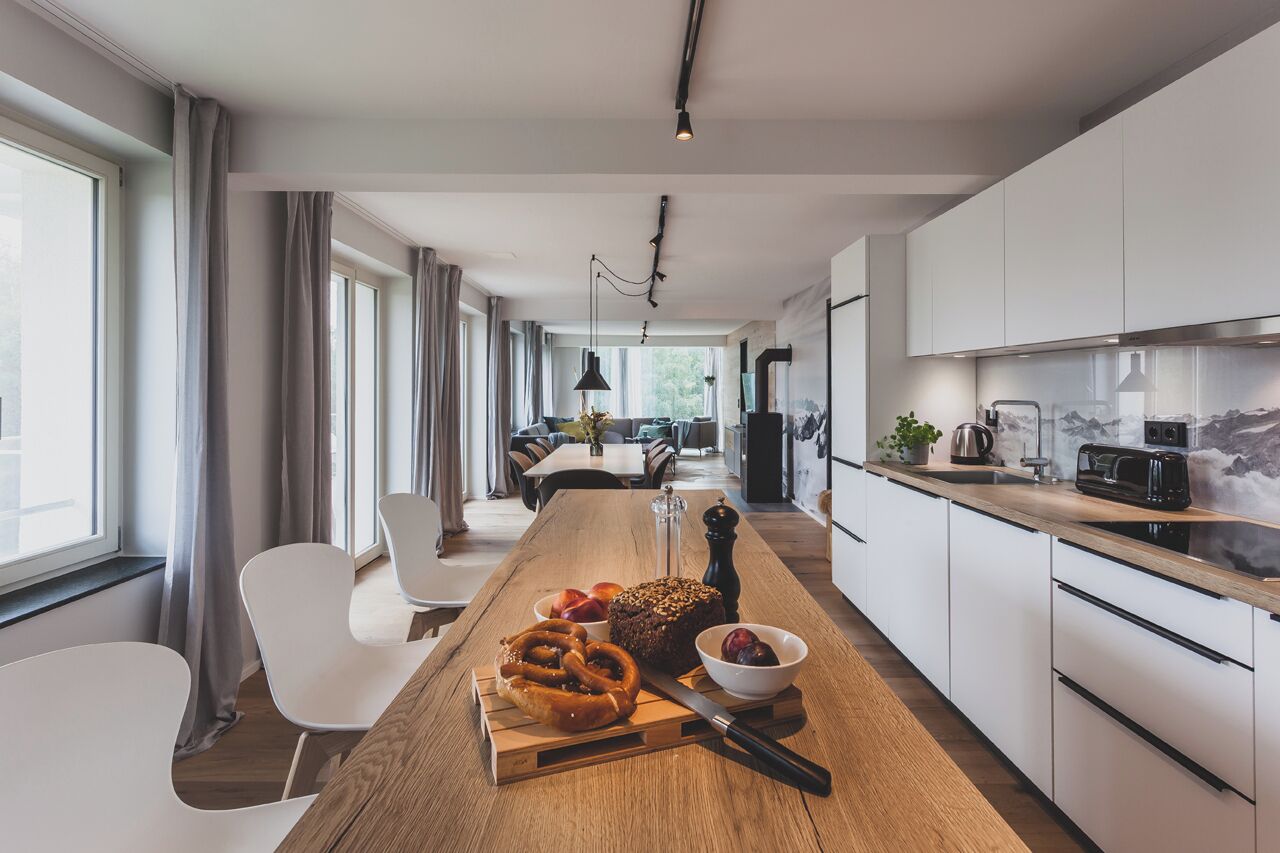 A modern kitchen with white cabinets, a wooden countertop, and a dining area with white chairs.