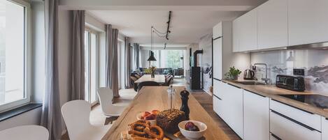 A modern kitchen with white cabinets, a wooden countertop, and a dining area with white chairs.