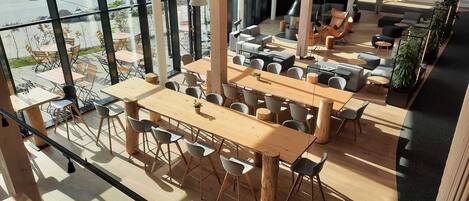 Un comedor moderno con mesas y sillas de madera, ventanas amplias y una chimenea central.