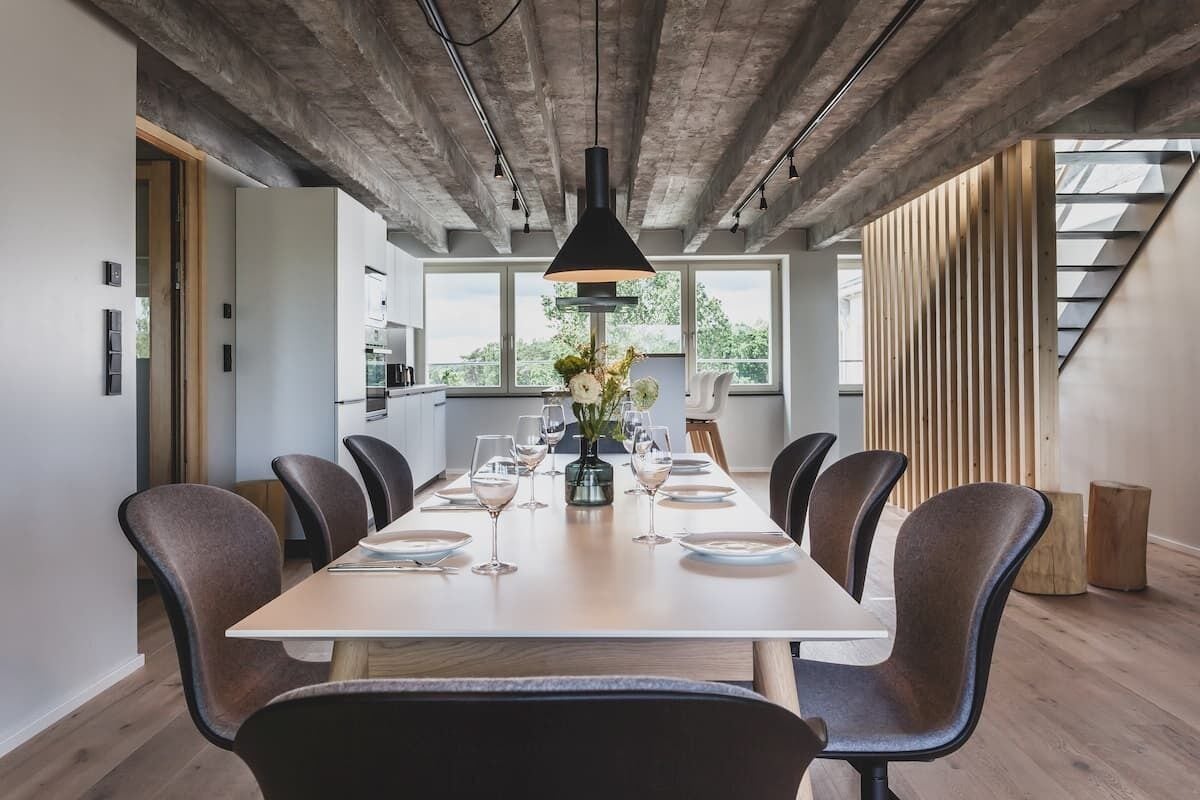 A modern dining area with a long table, dark chairs, and a hanging light fixture.