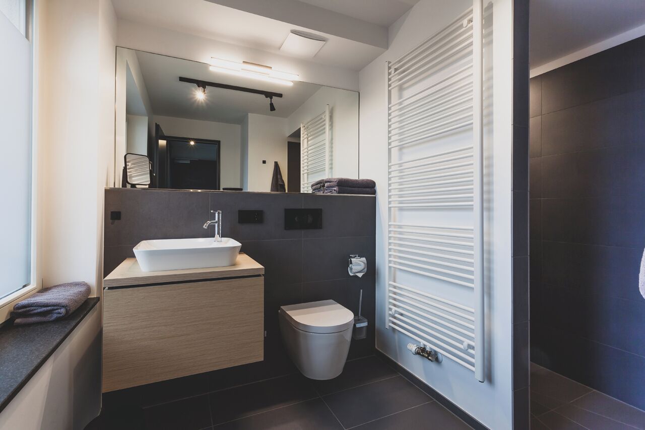 A modern bathroom with a large mirror, a sink, a toilet, and a radiator.