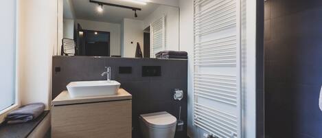 A modern bathroom with a large mirror, a sink, a toilet, and a radiator.