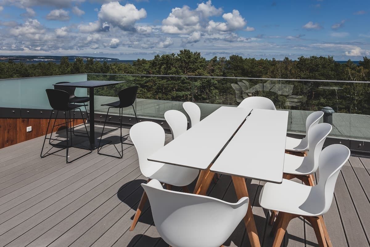 Una terraza en la azotea con barandilla de cristal, una mesa blanca y sillas modernas.