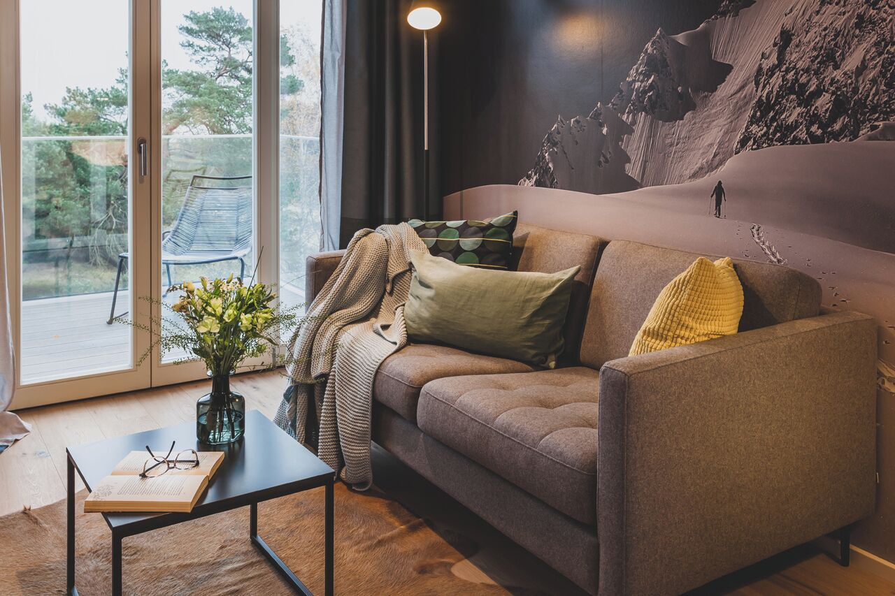 A modern living room with a sofa, a coffee table, and a view of a mountainous landscape through large windows.