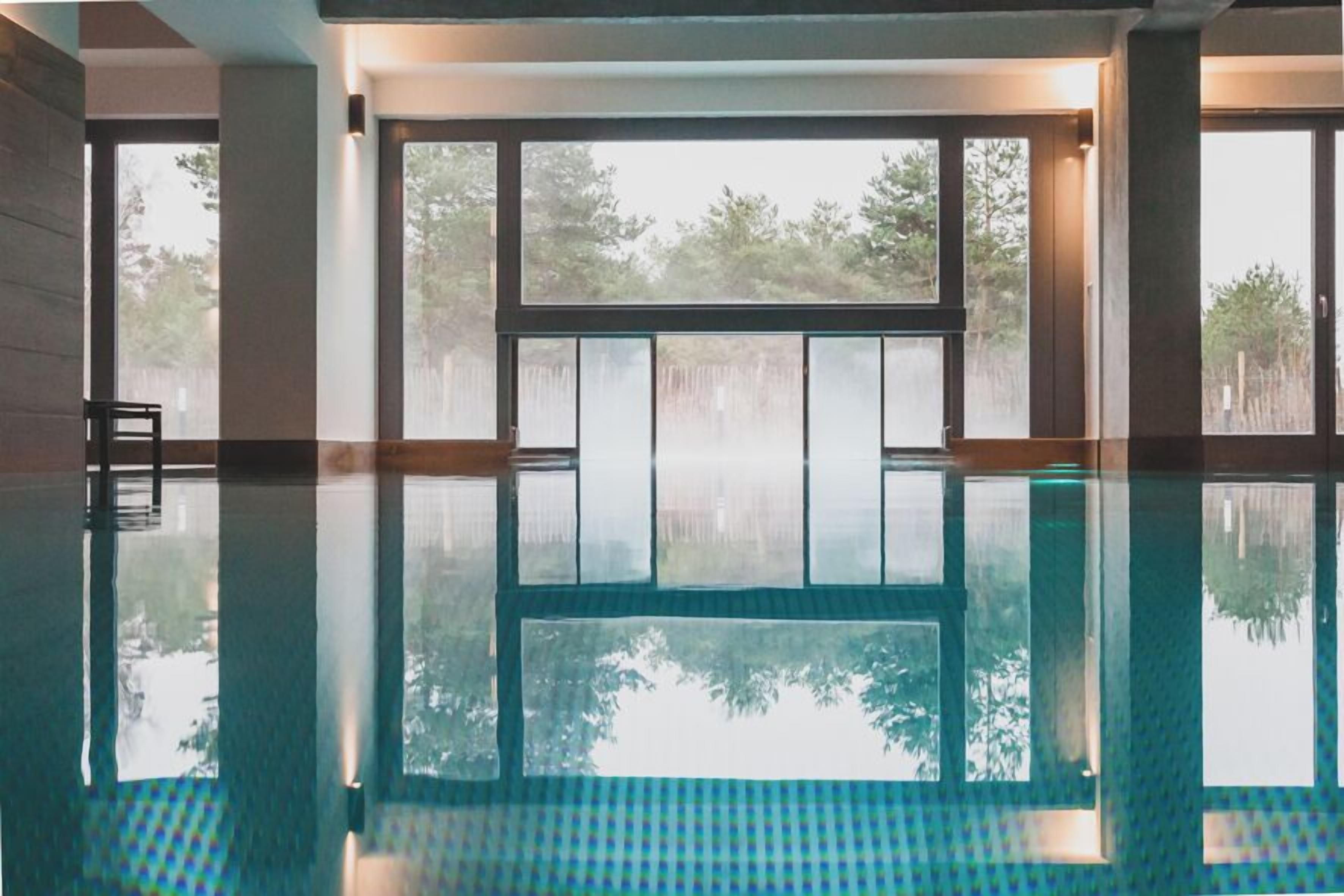 A clear indoor swimming pool with large windows and a view of trees outside.