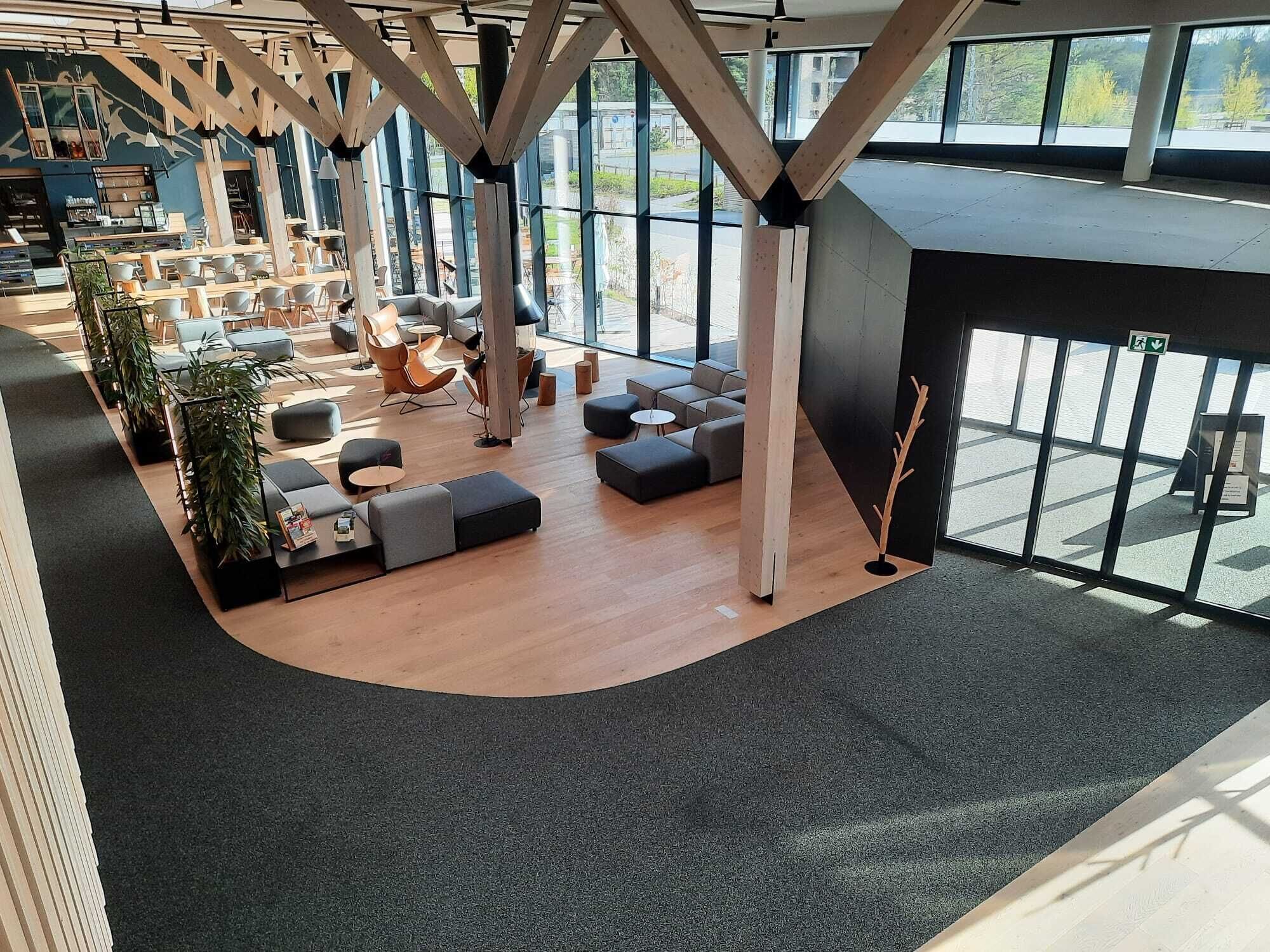 Ein modernes Interieur mit einer gebogenen Sitzecke, großen Fenstern und freiliegenden Holzbalken.