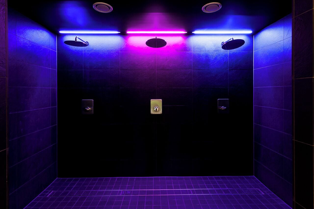 A modern, dimly lit elevator with purple lighting, featuring two hand dryers and a control panel.