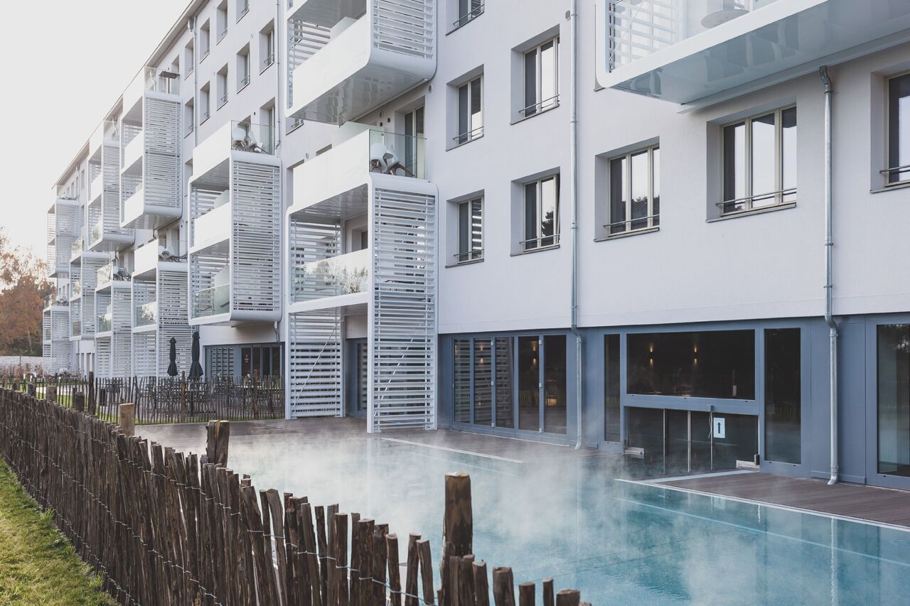 Un immeuble résidentiel moderne à plusieurs étages, doté de balcons, d’une piscine et d’une clôture en bois.