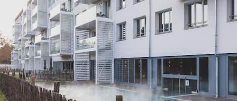 A modern multi-story residential building with balconies, a swimming pool, and a wooden fence.