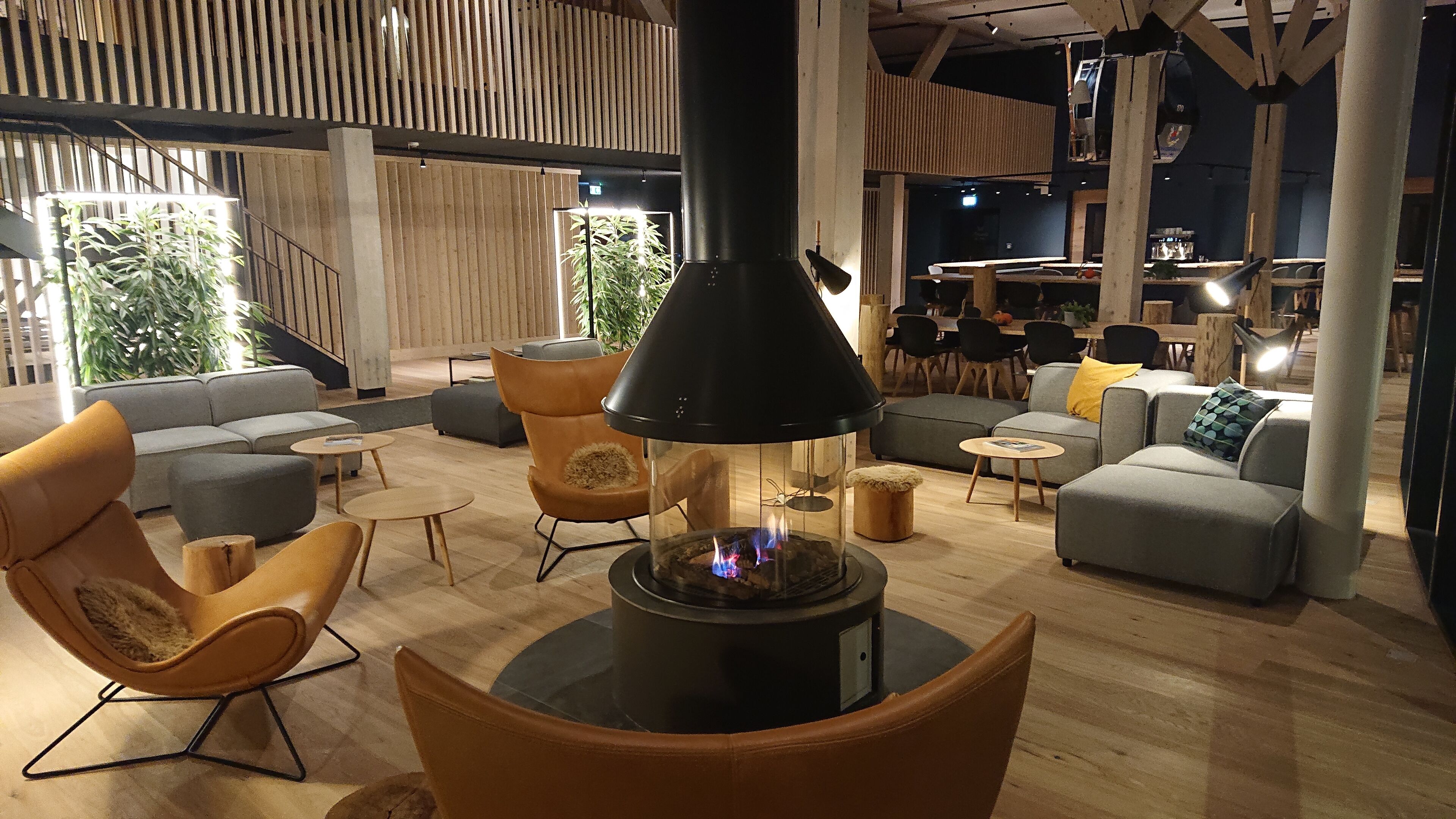 Un interior moderno con una estufa de leña en el centro, sofás y un comedor.