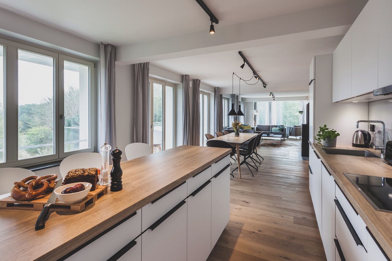 A modern kitchen with a wooden countertop, white cabinets, and a dining area with a table and chairs.