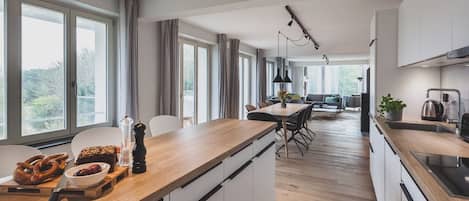 Eine moderne Küche mit Holzarbeitsplatte, weißen Schränken und einem Essbereich mit Tisch und Stühlen.