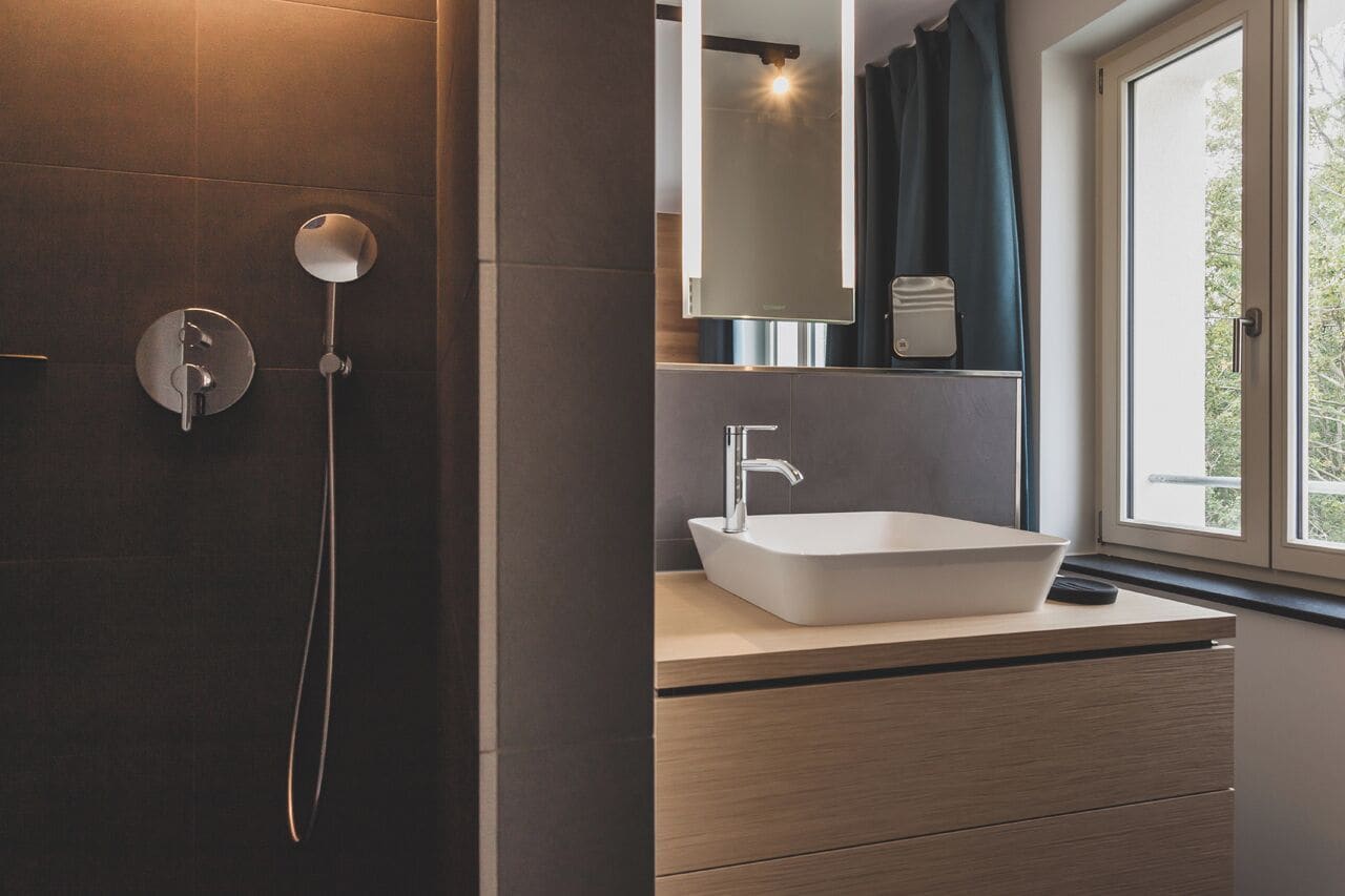 A modern bathroom with a large window, a white sink, and a shower area.