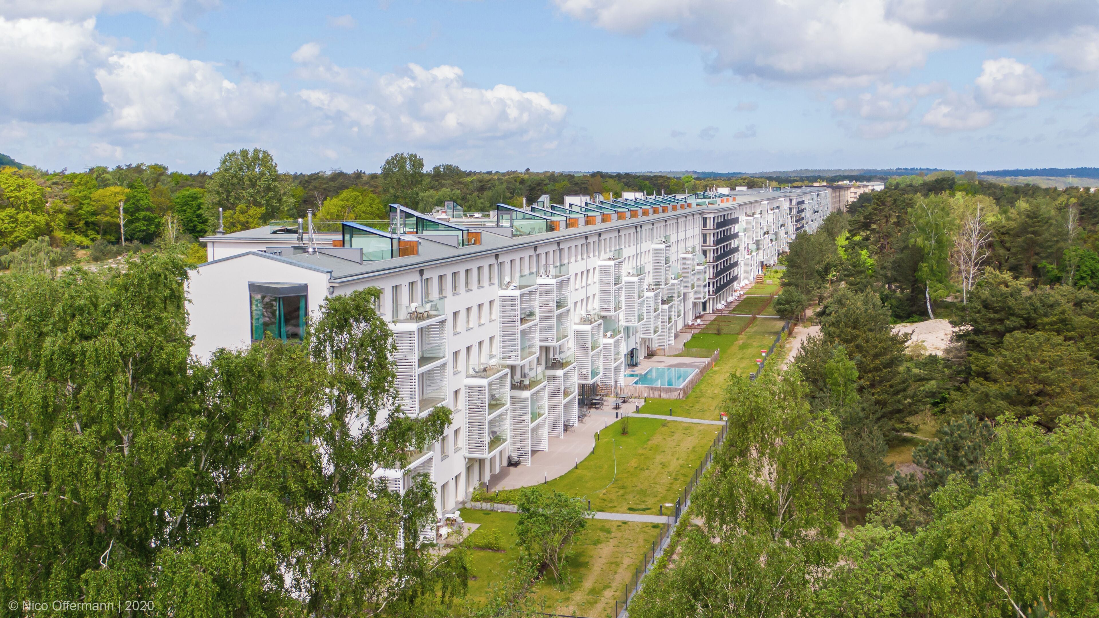 Ein modernes Hotel mit mehreren Etagen, einem Außenpool und üppiger Grünanlage rund um das Anwesen.