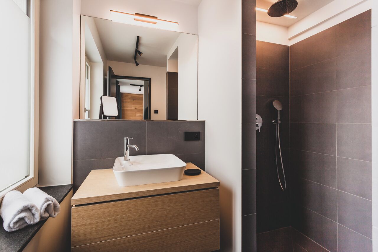 Un baño moderno con un lavamanos rectangular, tocador de madera y ducha a ras de suelo.
