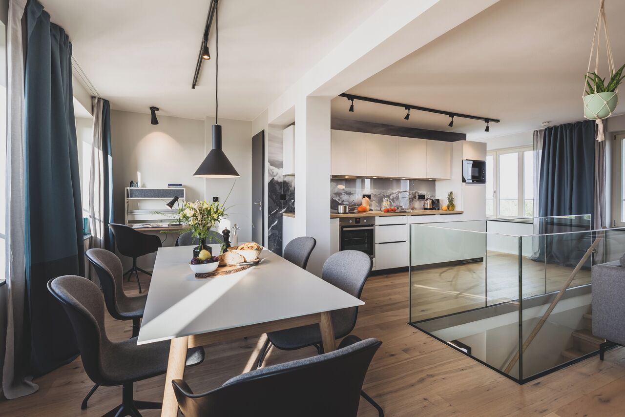 Una cocina moderna con armarios blancos, una isla central y un comedor con mesa y sillas blancas.
