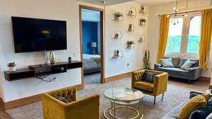 A modern living room with a flat-screen TV, yellow armchairs, a grey sofa, and a glass coffee table. - 3 bedroom, 2 bath apartment. In Castle! With pool! Close to GR and lakeshore (Grandville)