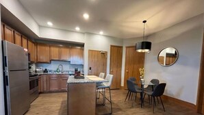 A modern kitchen with wooden cabinets, a central island, and a dining area with a round table and chairs. - 3 bedroom, 2 bath apartment. In Castle! With pool! Close to GR and lakeshore (Grandville)