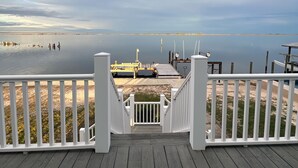 A wooden deck with a white railing leading to a sandy beach.