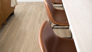 A modern kitchen with a white countertop, brown leather chairs, and a wooden floor.