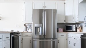 A modern kitchen with white cabinets, stainless steel appliances, and a wooden floor.