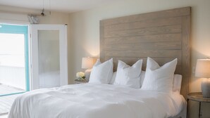 A large bed with white linens, a wooden headboard, a ceiling fan, and a view of a balcony.