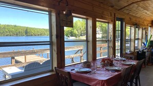 Una cabaña de madera con una mesa de comedor para dos personas, con vistas a un lago.