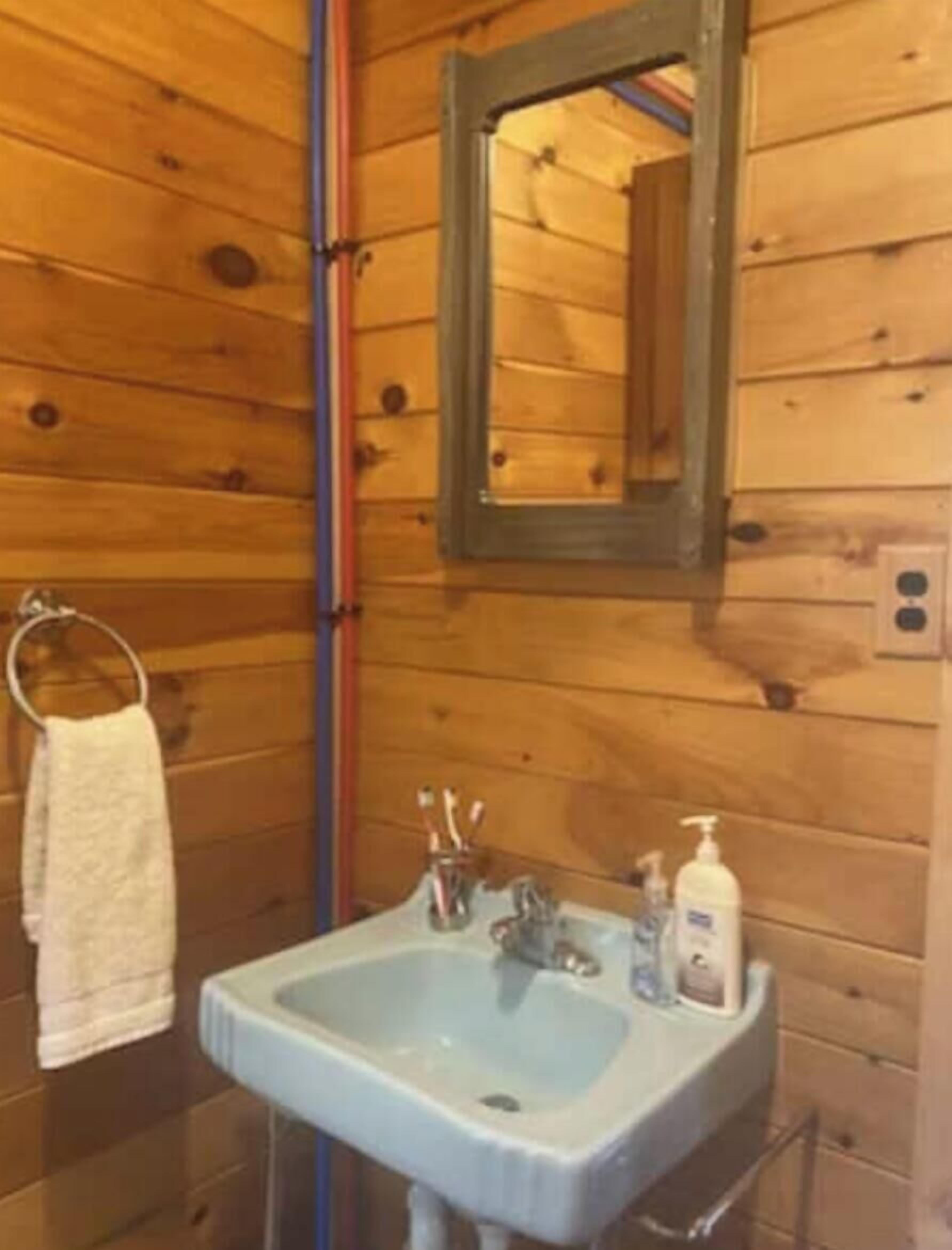 A wooden cabin bathroom with a sink, mirror, towel rack, and toiletries.
