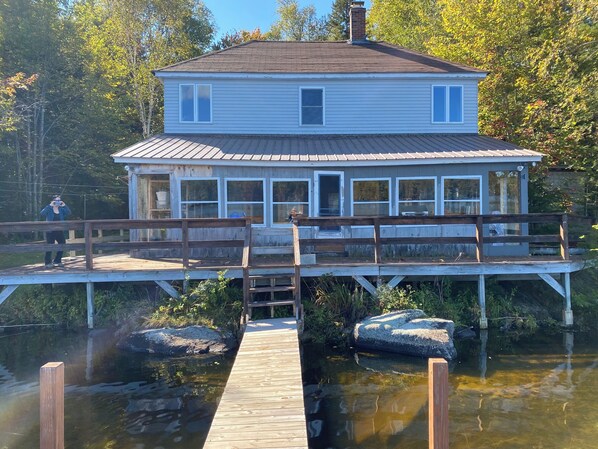 A two-story house with a dock extending into a body of water, surrounded by trees. - Quiet cabin on Center Pond. (Lincoln)